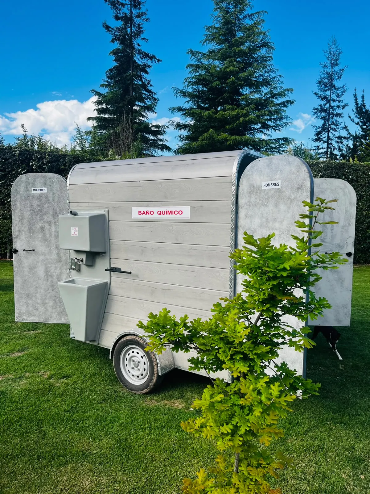 Carro con baño cuádruple y lavamanos exterior instalado en un jardín para eventos